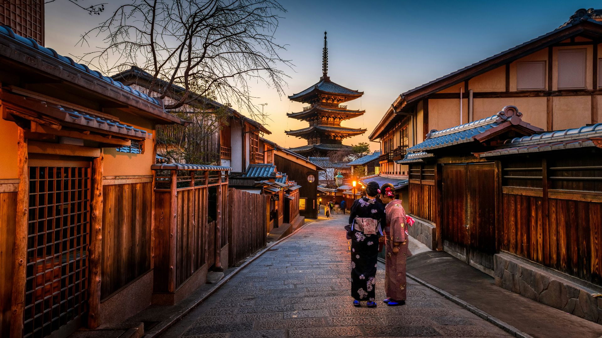 two women in purple and pink kimono standing on street