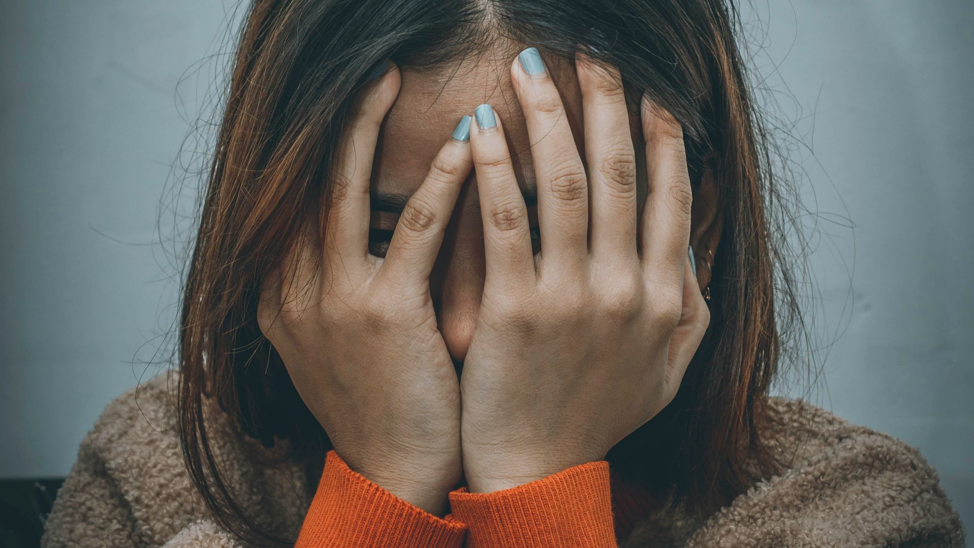 woman in brown sweater covering her face with her hand