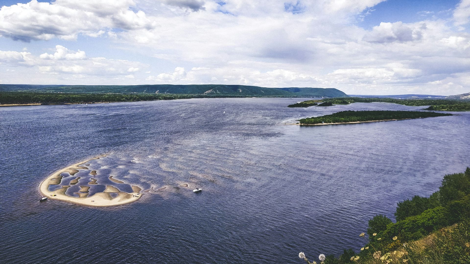 green grass field near body of water under white clouds and blue sky during daytime