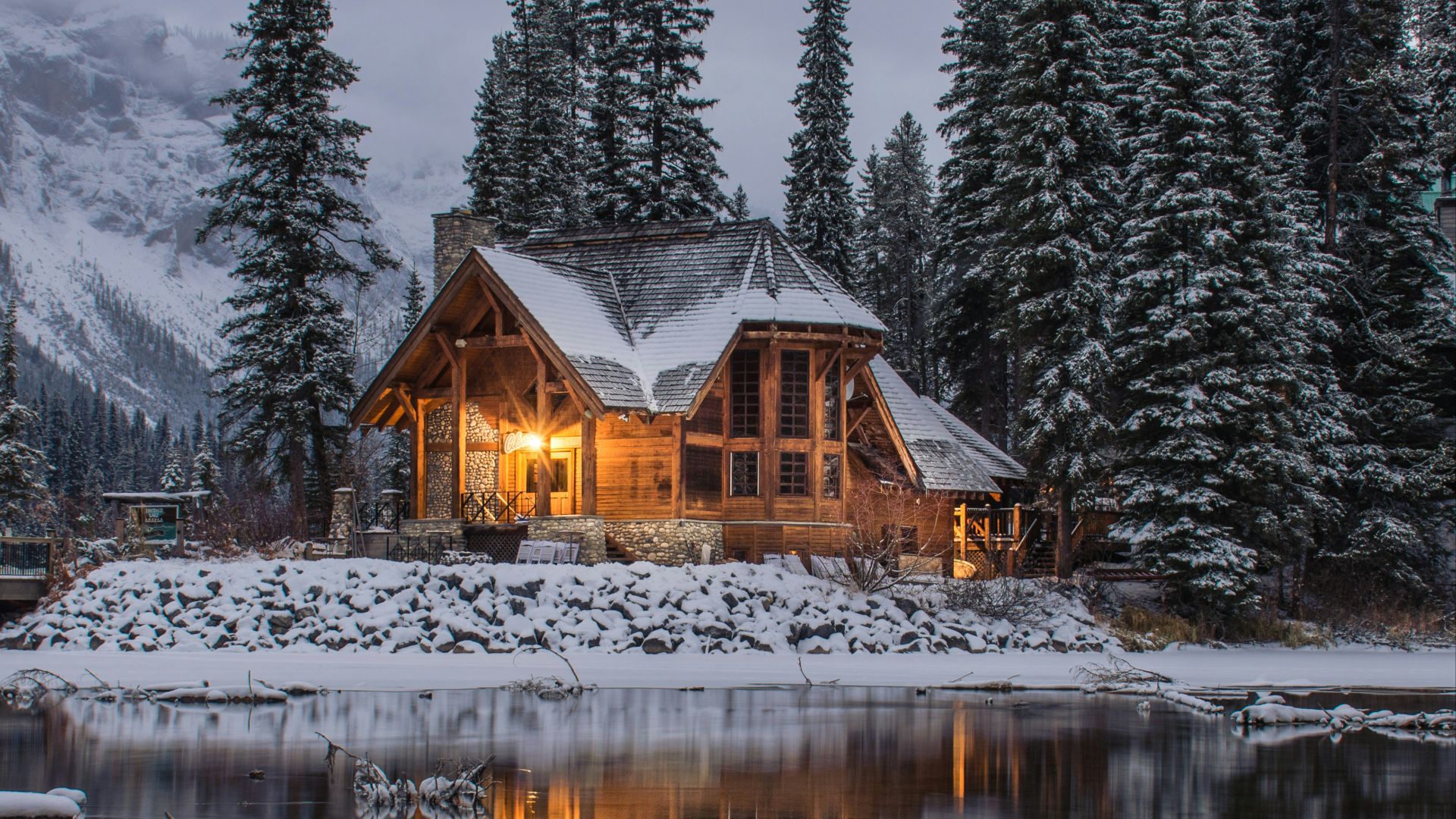 wooden house near pine trees and pond coated with snow during daytime