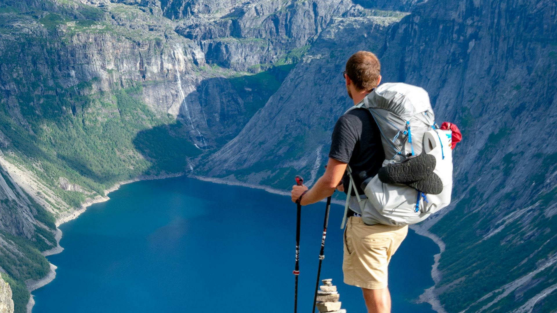 man standing on rock looking towards lake