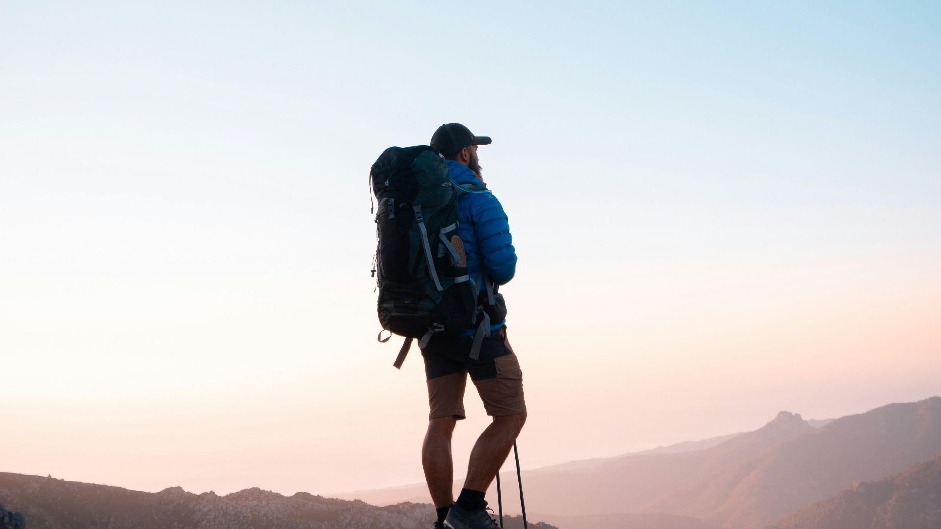 man in black jacket and blue denim shorts with black hiking backpack standing on mountain during