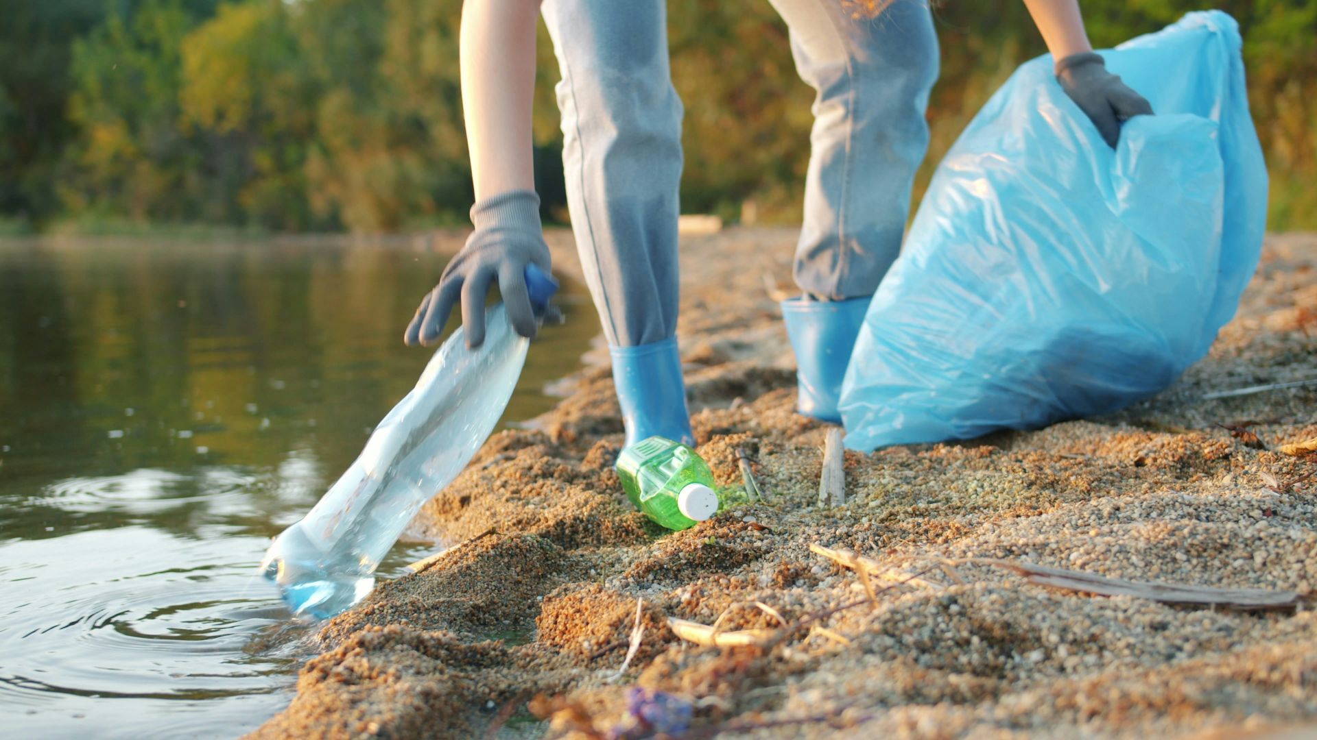 Person picking up plastic bottle near water
