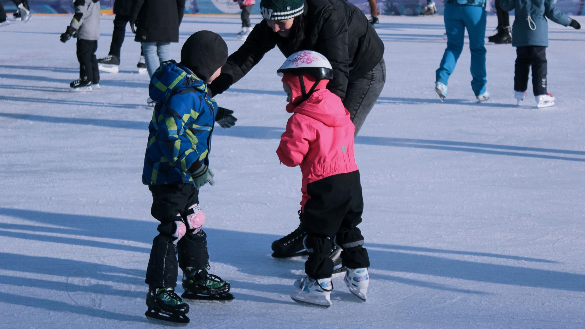 2 children in red jacket and black pants playing ice hockey