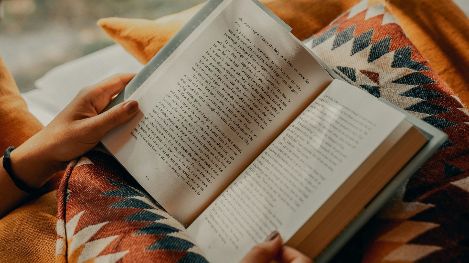 person reading book on brown and beige textile