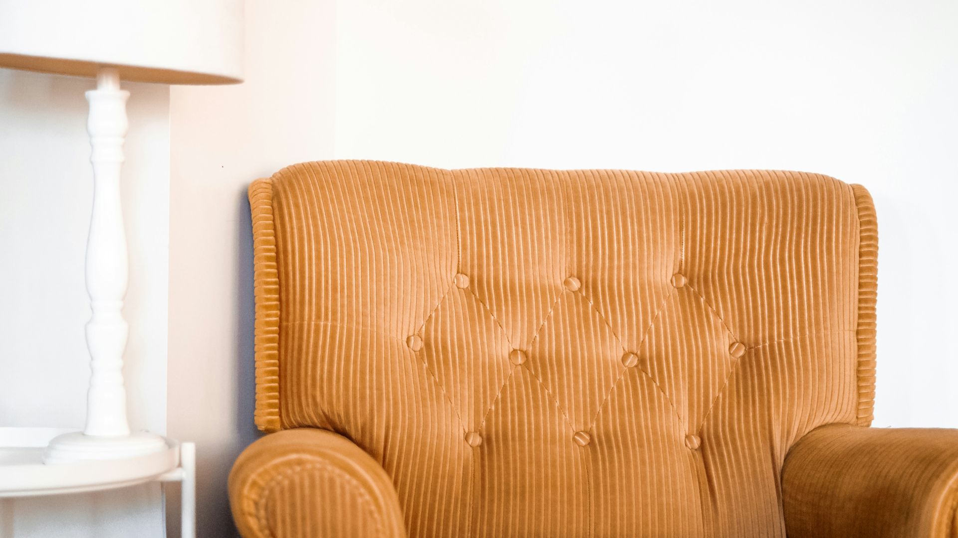 tufted brown fabric sofa chair beside white table lamp on white end table
