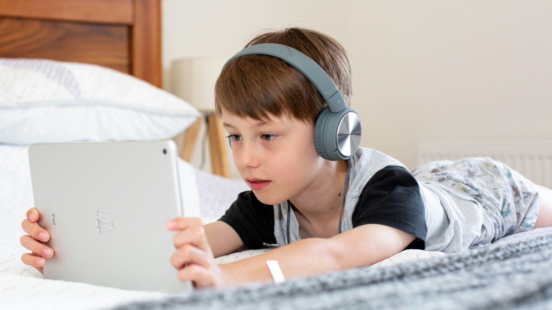 boy in blue shirt wearing headphones lying on bed