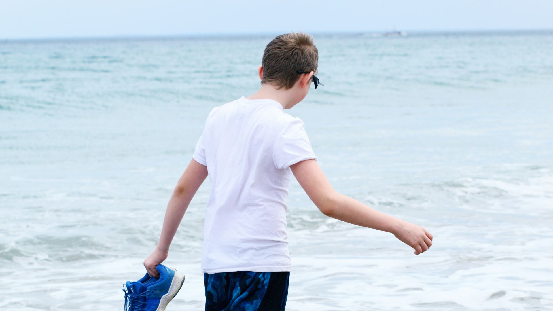 boy in white t-shirt and blue shorts running on beach during daytime