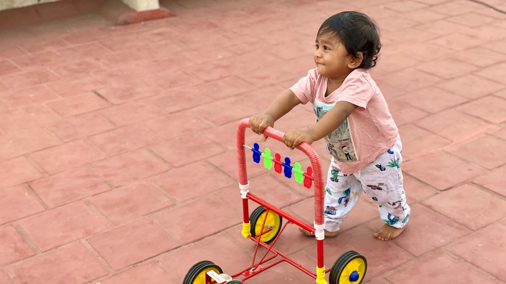 girl in white and pink floral dress riding red and yellow trike