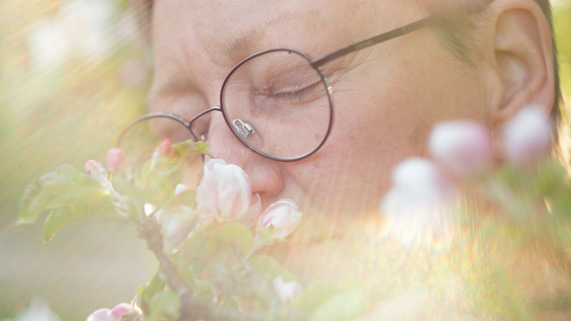 a woman with glasses is smelling a flower