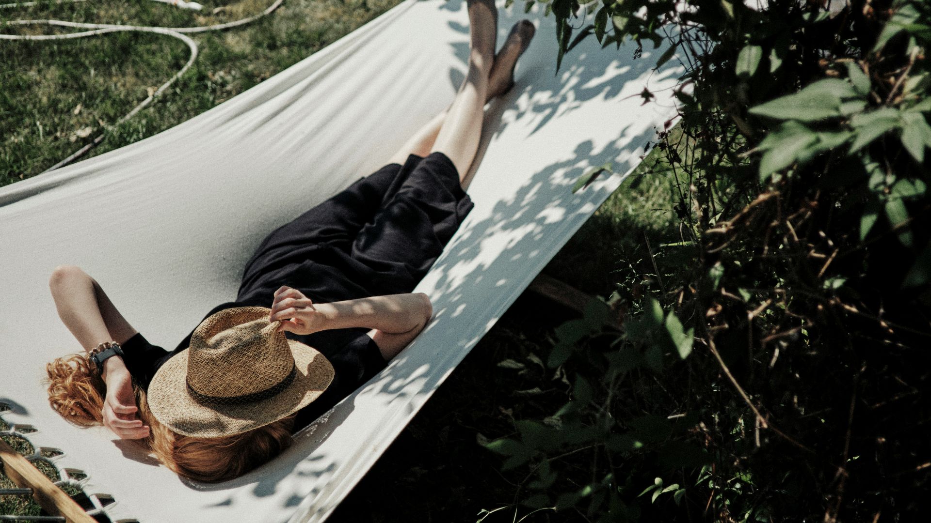 A man laying in a hammock with a hat on