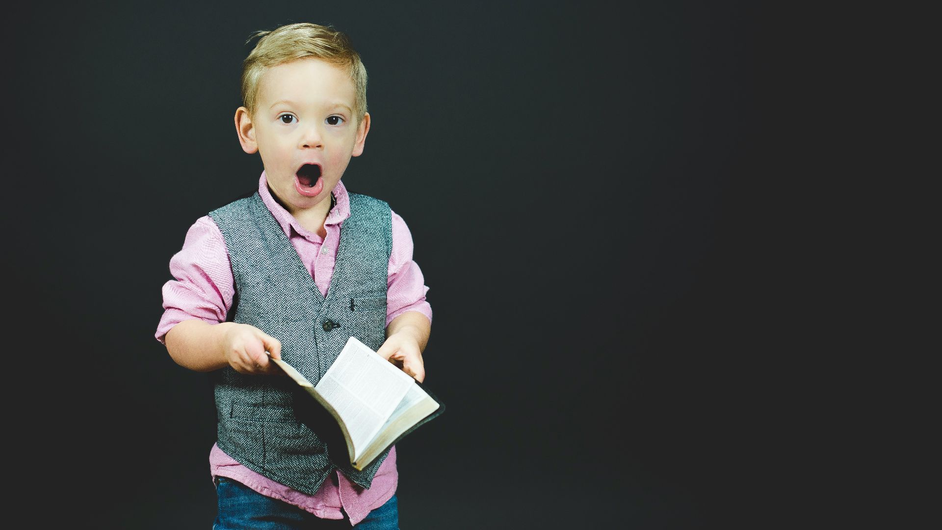 boy wearing gray vest and pink dress shirt holding book