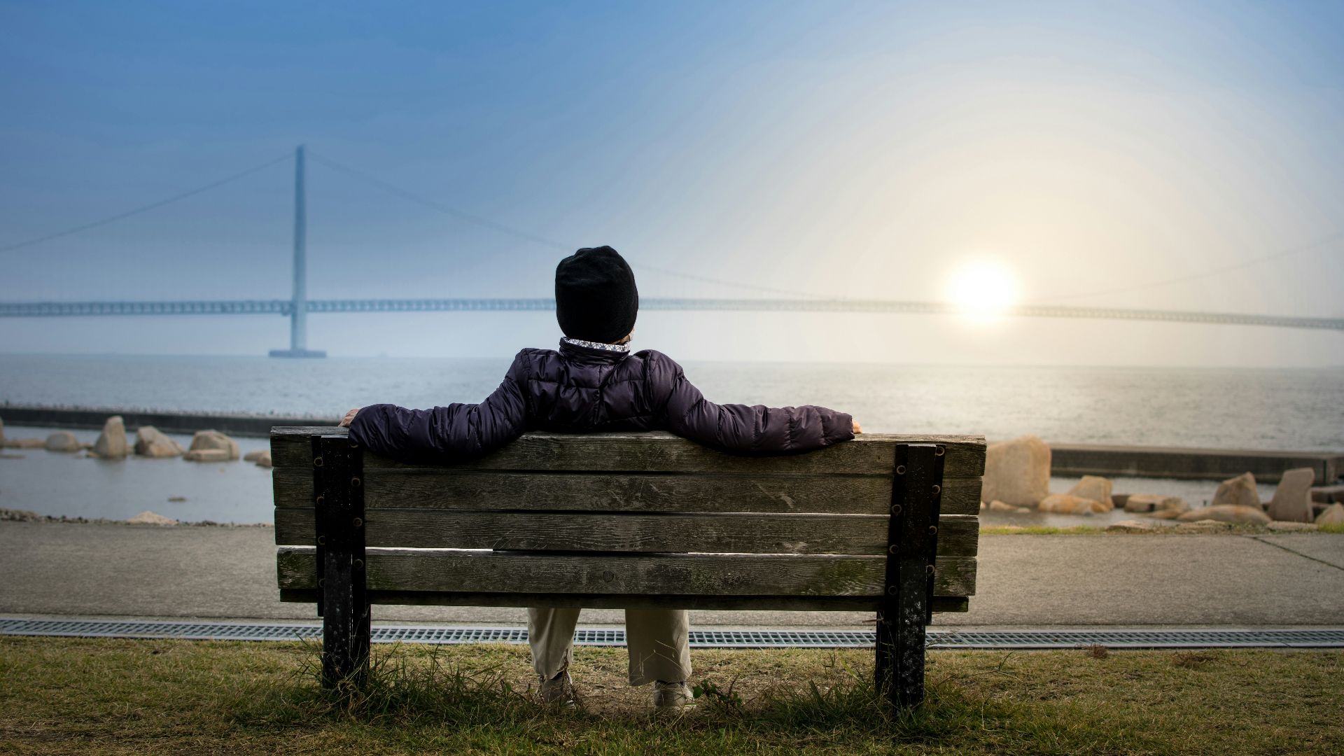 person sitting on bench facing suspension bridge