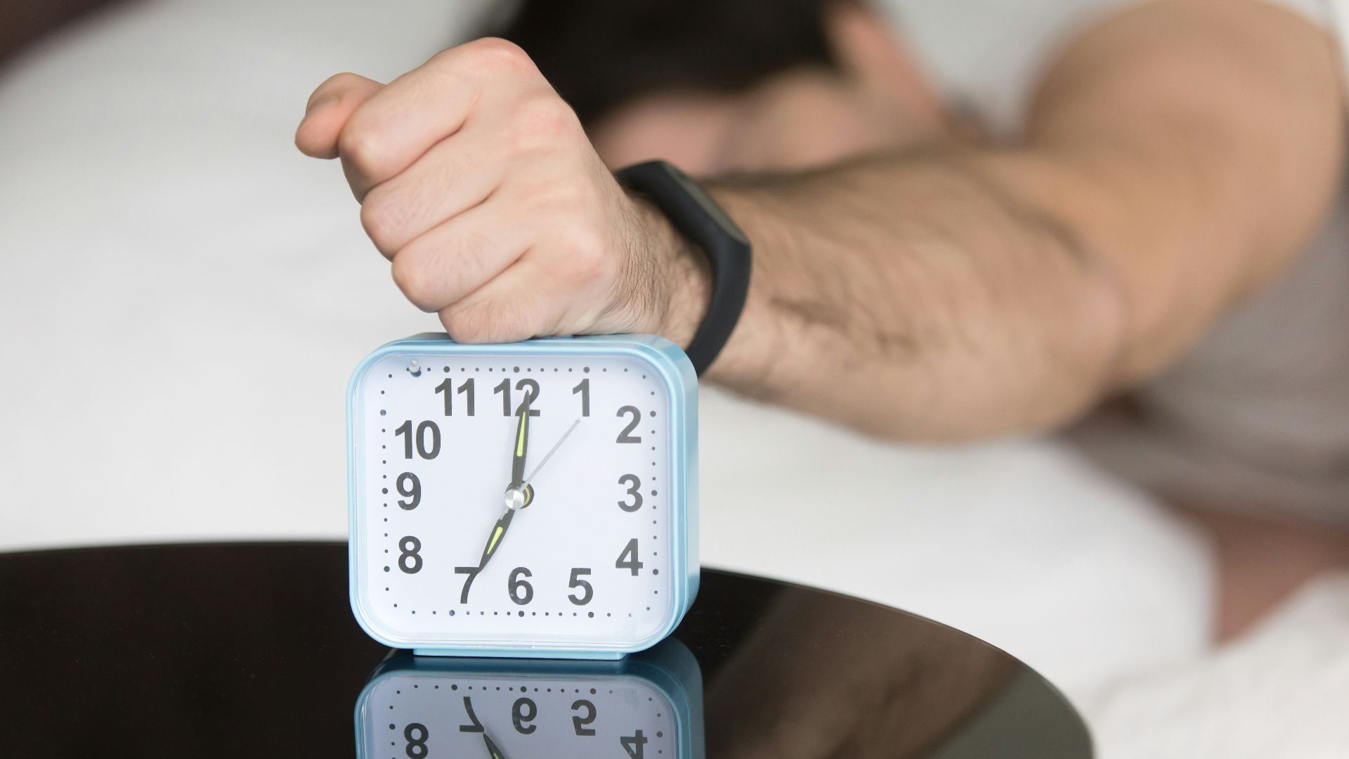 A man laying in bed with a clock on top of him