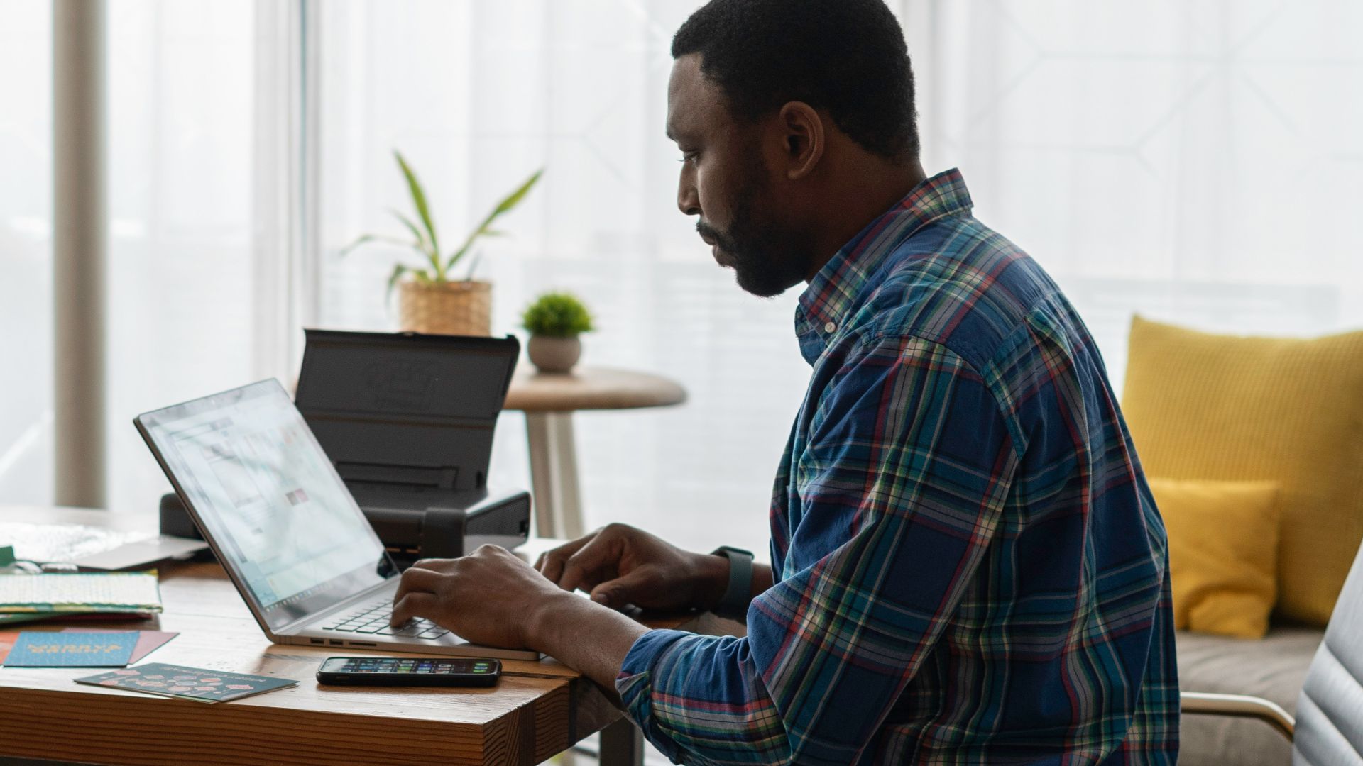 man in blue and white plaid dress shirt sitting on chair using laptop computer