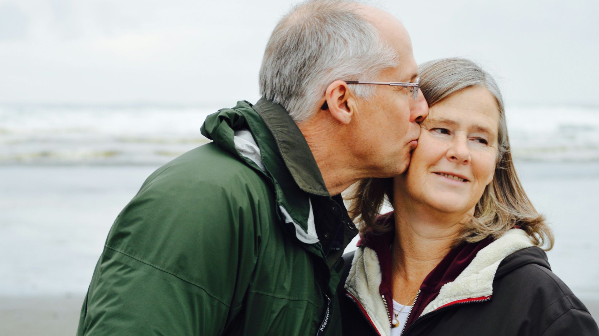 man kissing woman on check beside body of water