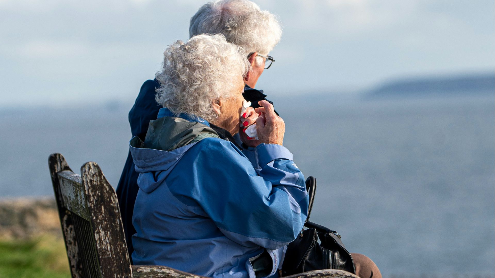 man and woman sitting on gray wooden bench viewing blue sea during daytime
