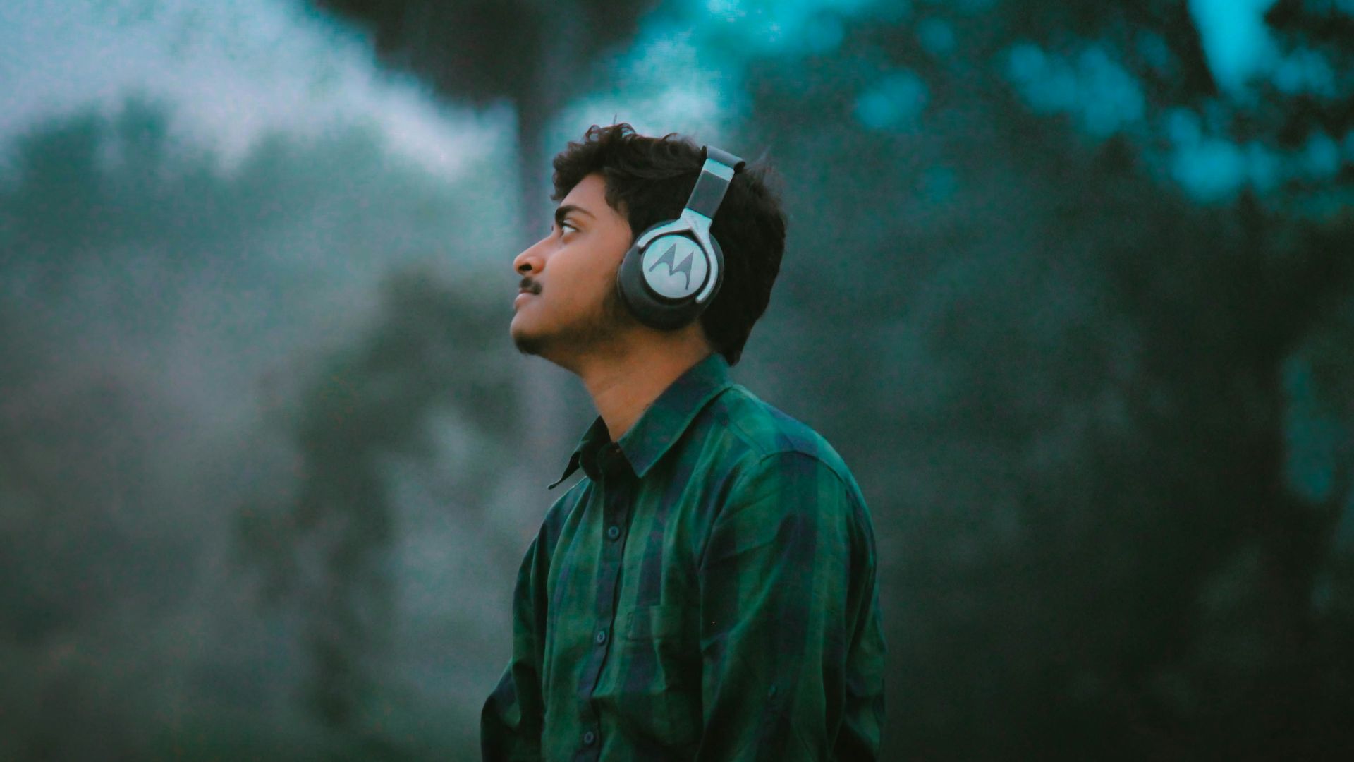 man in green and black plaid dress shirt wearing black and white headphones