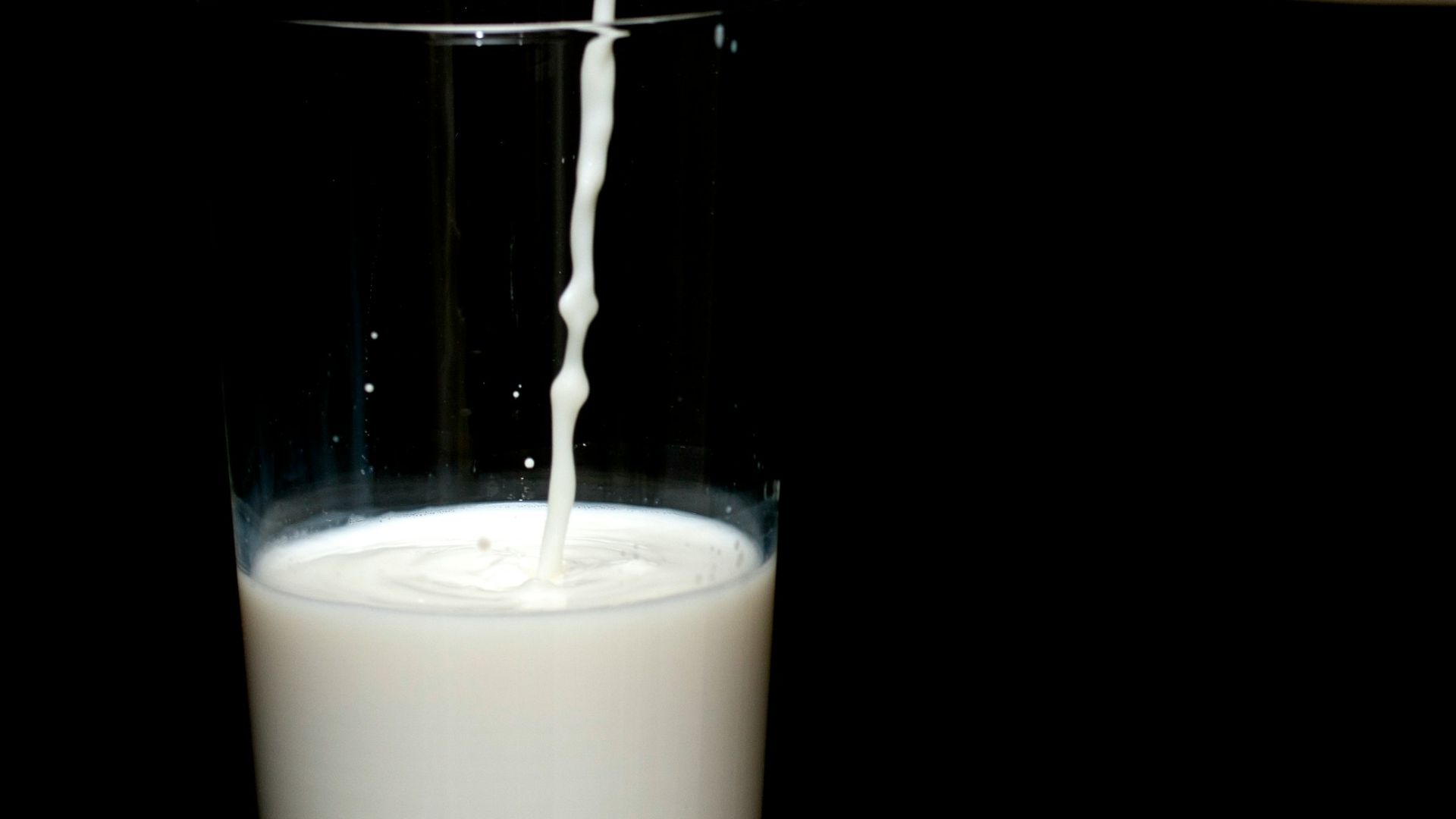 person pouring milk on clear drinking glass