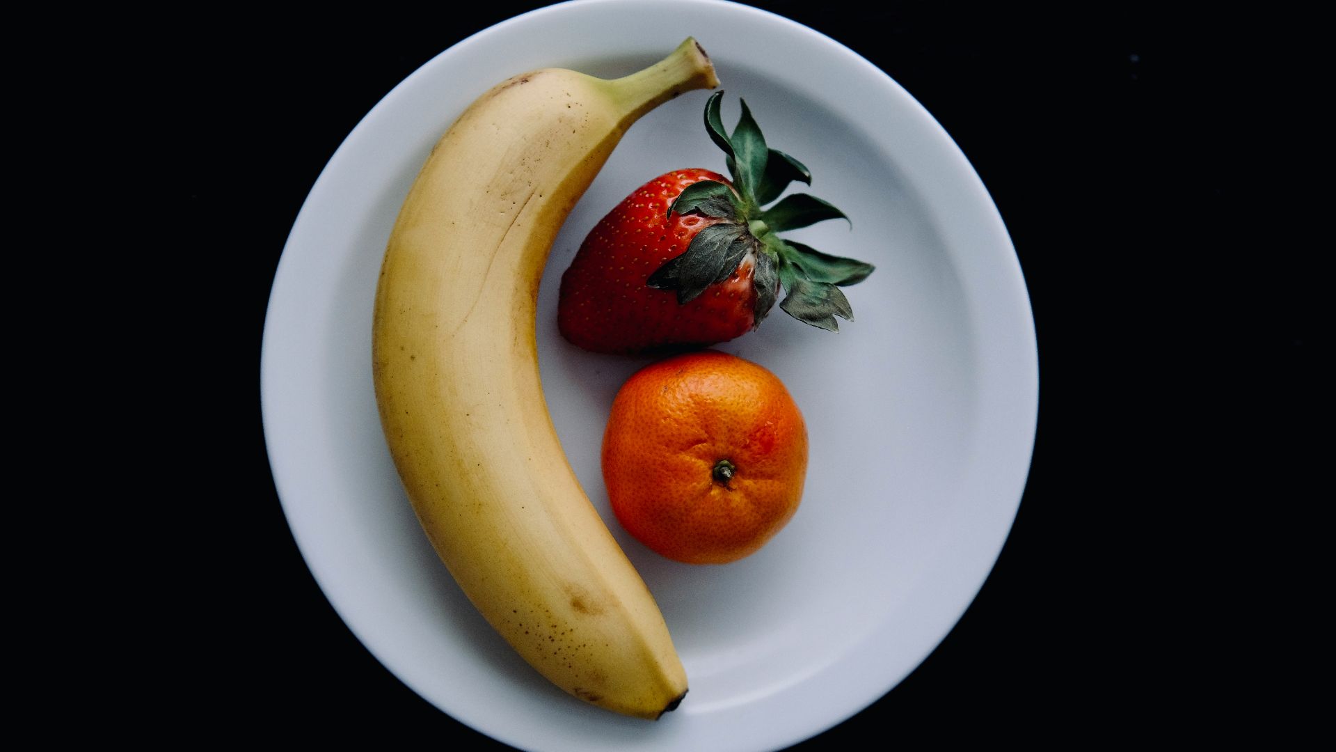 a banana, orange and strawberry on a white plate