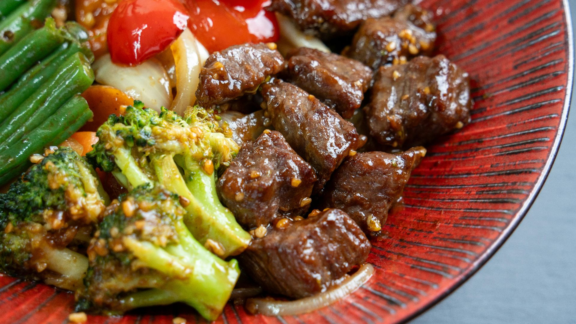 Beef and broccoli stir-fry with vegetables on a red plate
