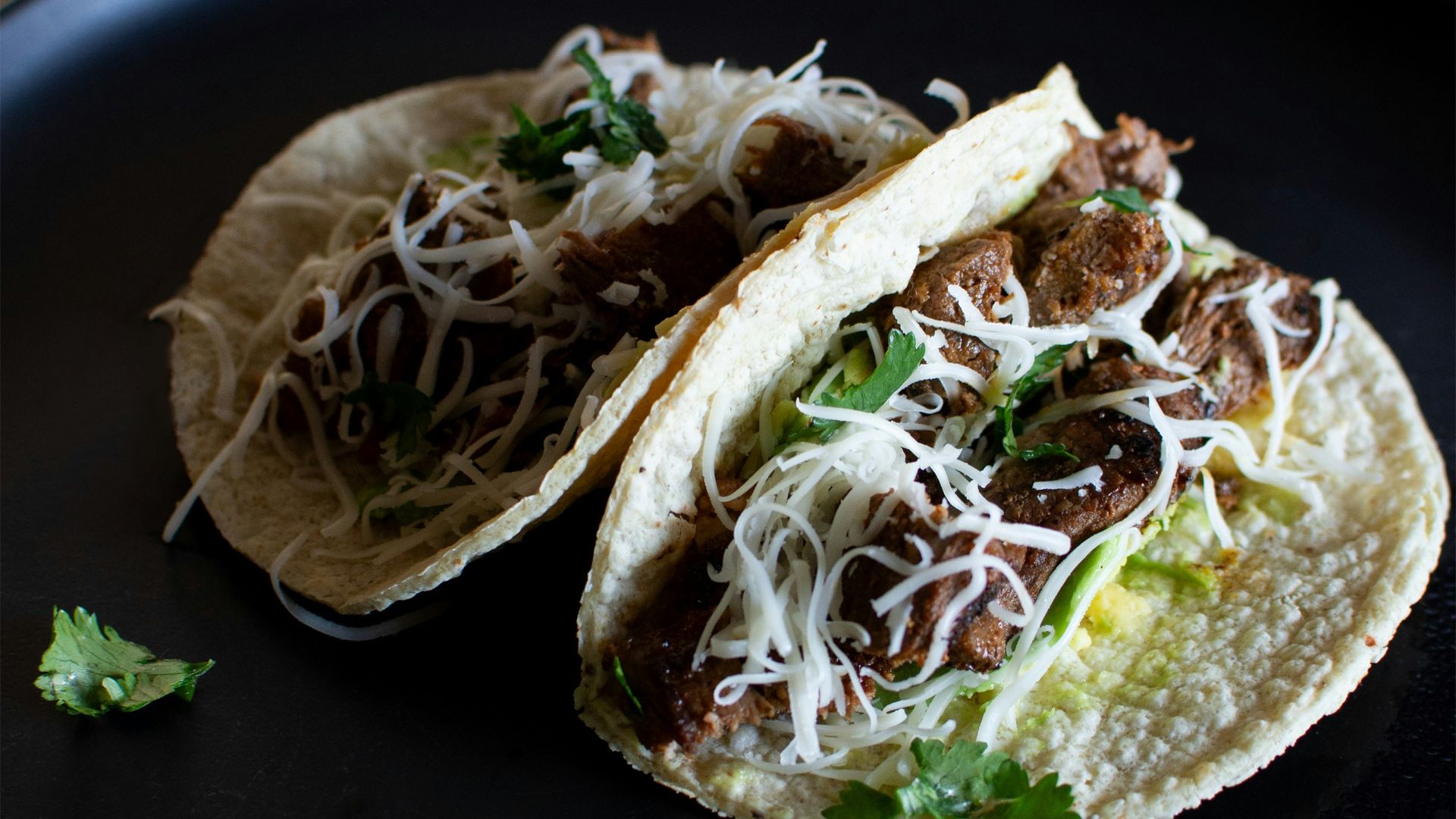 two tacos on a black plate with a lime