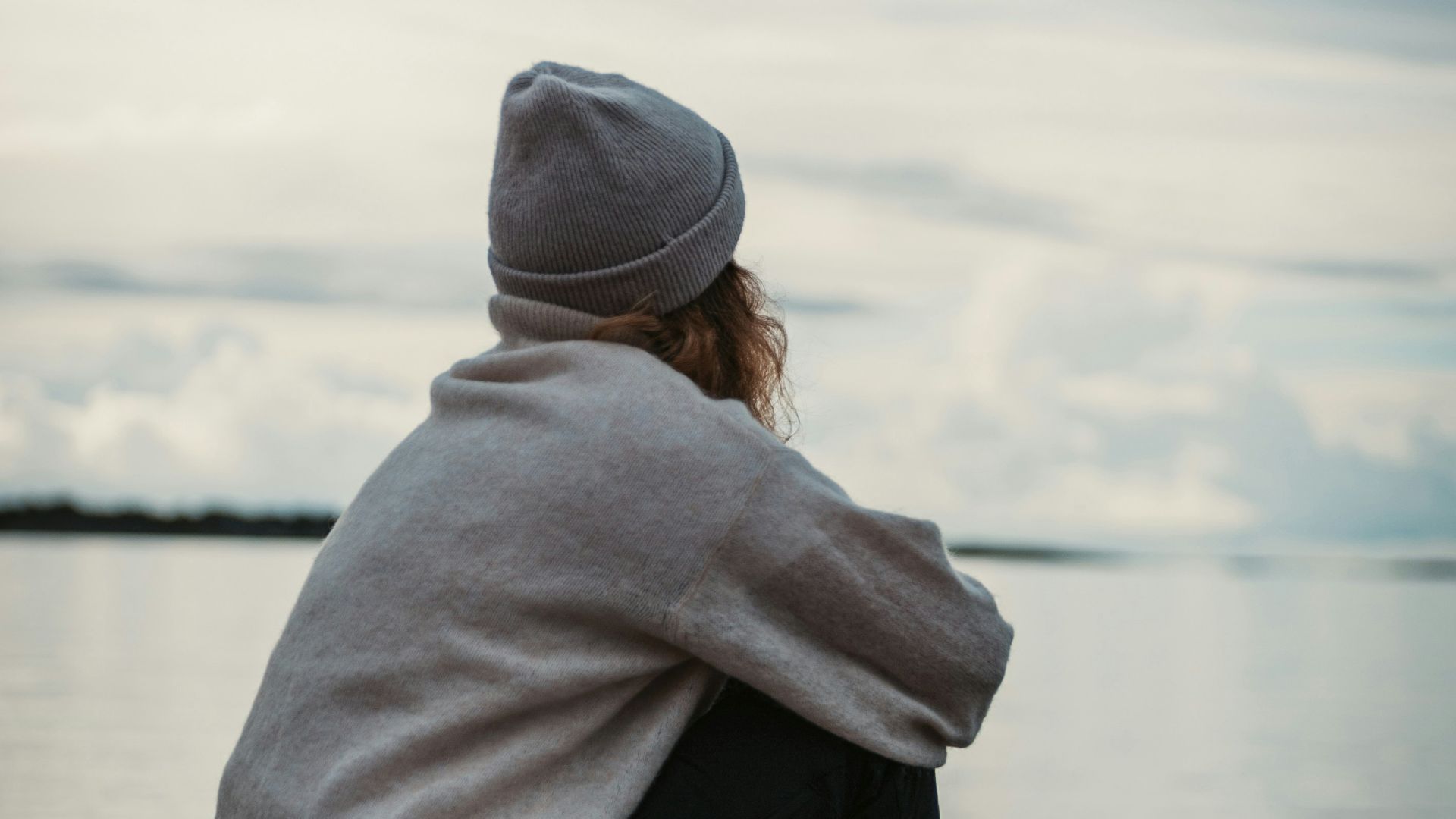 person in gray hoodie and black pants sitting on brown wooden dock during daytime