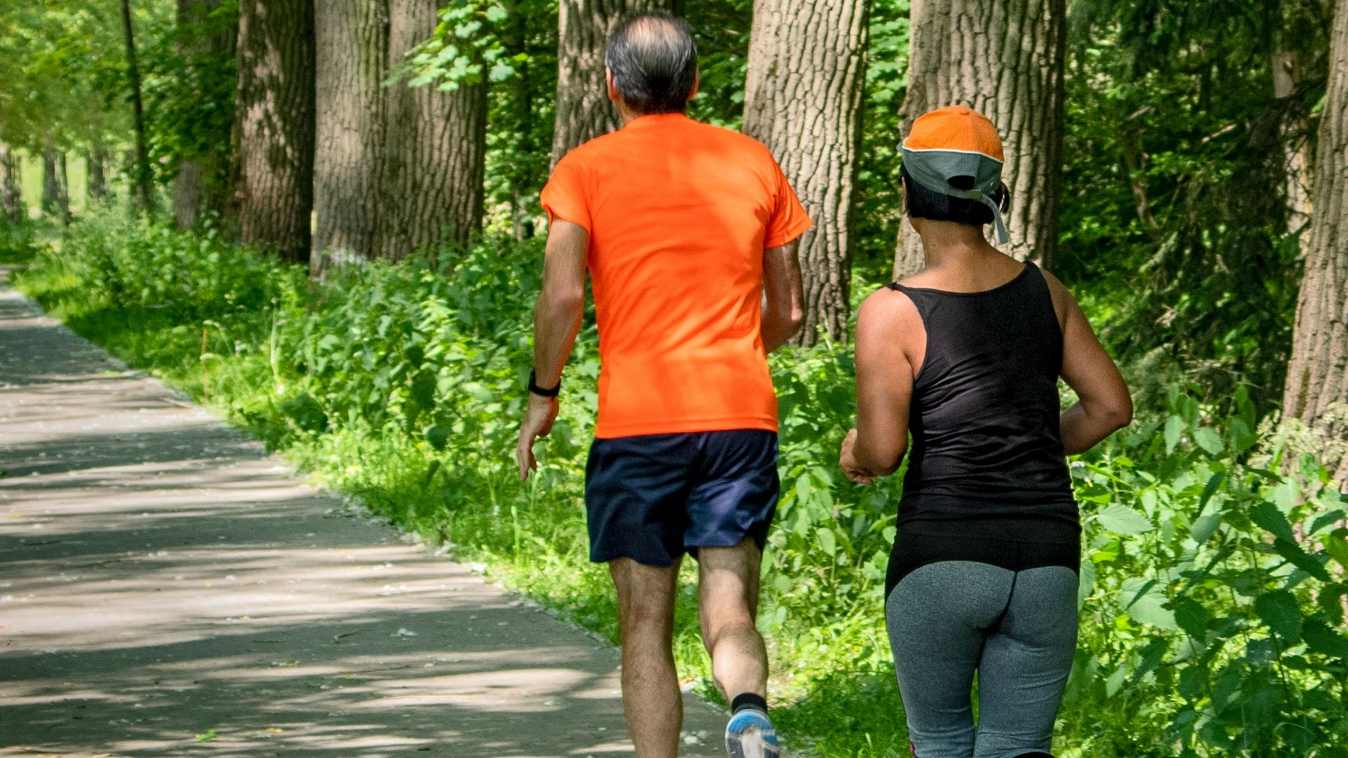 man in orange t-shirt and gray pants with blue shoes walking on pathway