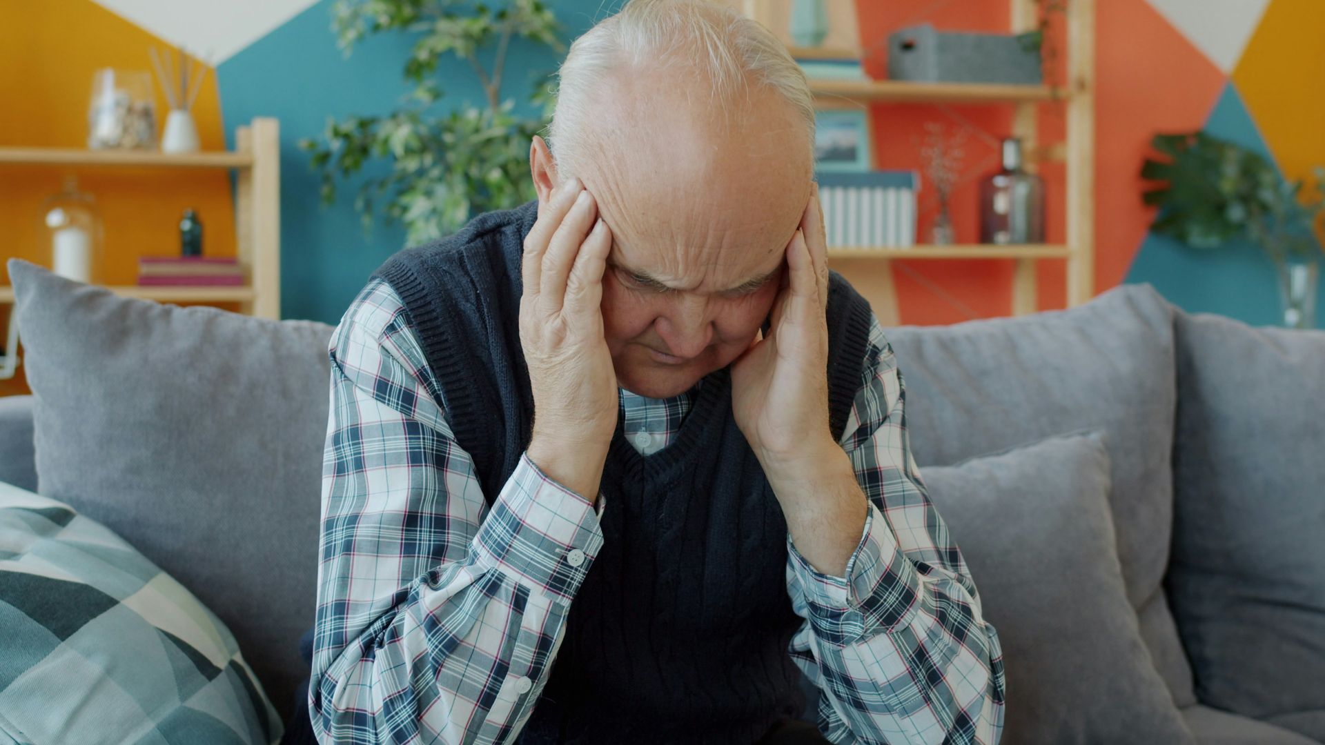 Elderly man holding head in discomfort on couch