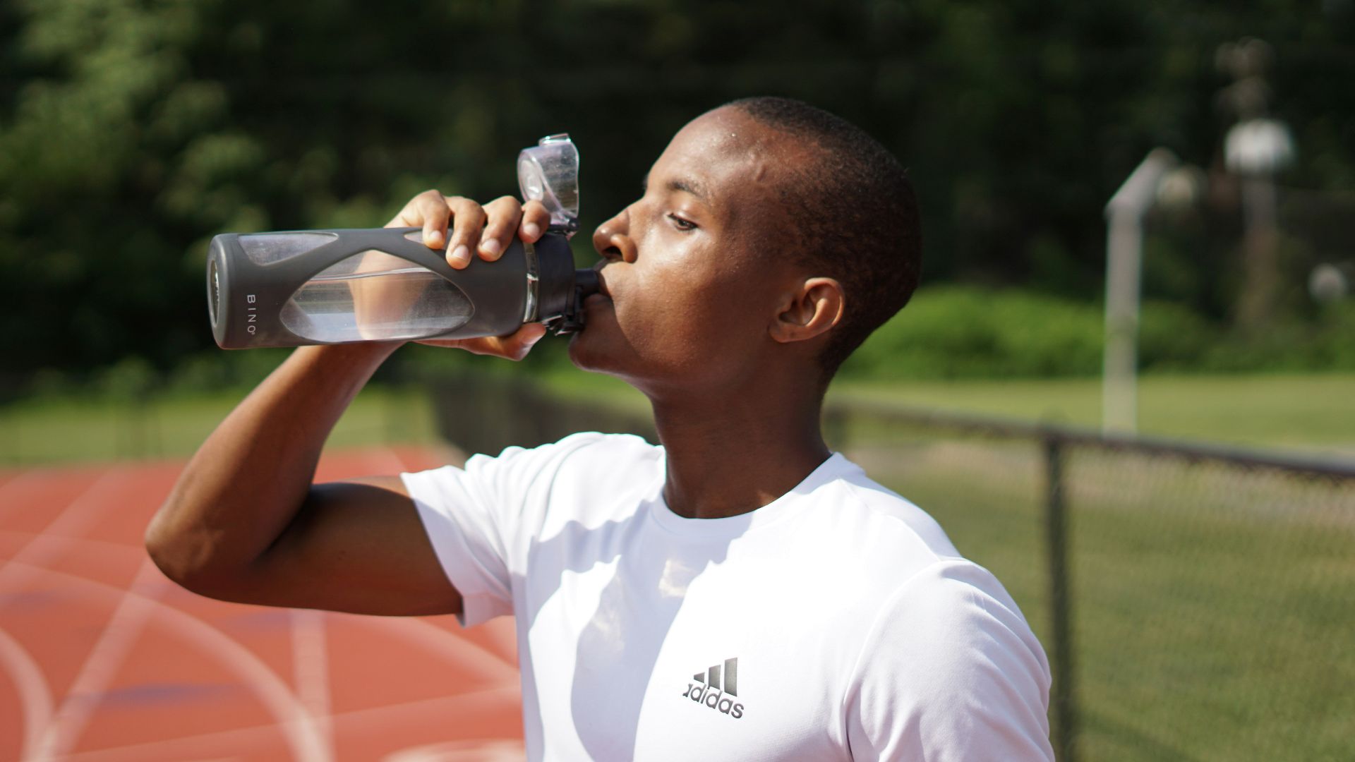 man in white crew neck t-shirt drinking from black sports bottle