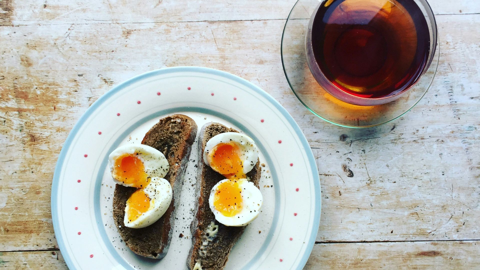 boiled eggs and toast on white ceramic plate near clear glass teacup filled with brown liquid