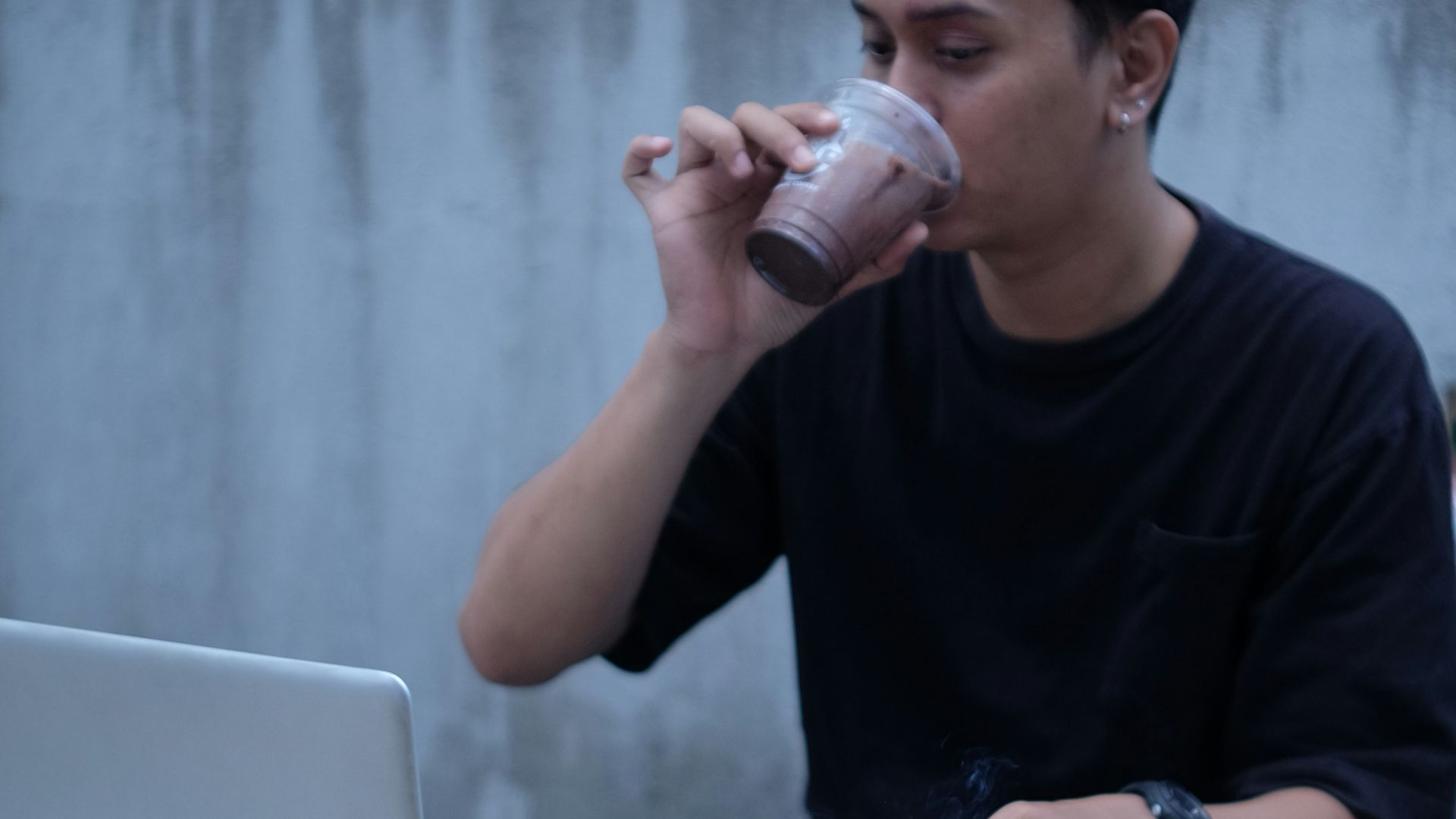 a man drinking from a cup while using a laptop