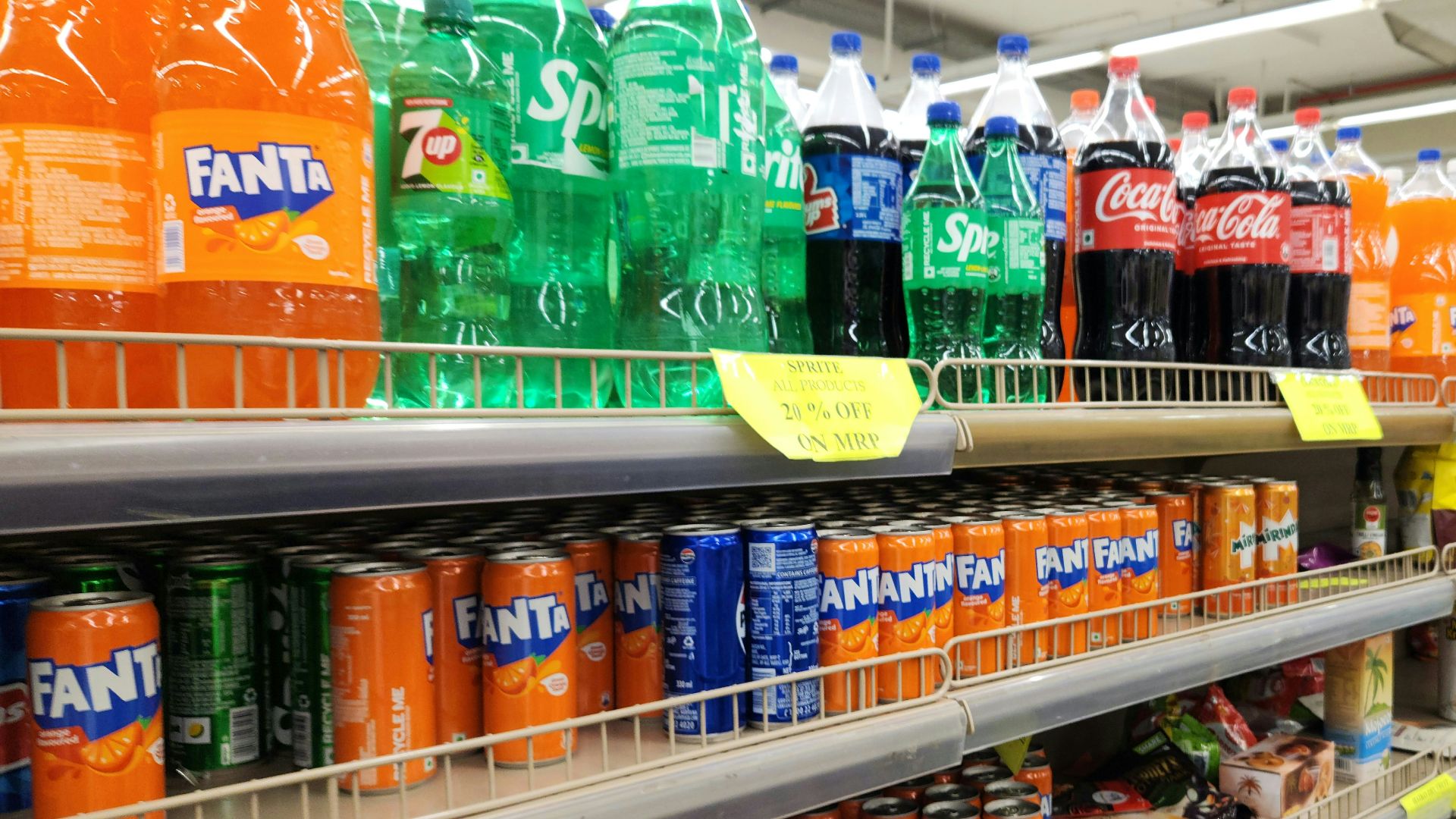 Soda bottles and cans are stocked on supermarket shelves.