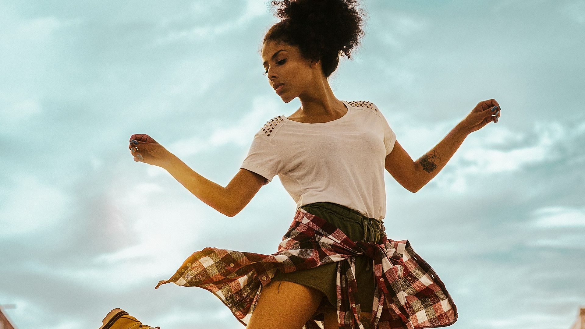 woman wearing white crew-neck shirt and black shorts standing on one foot with hands lifted to the side