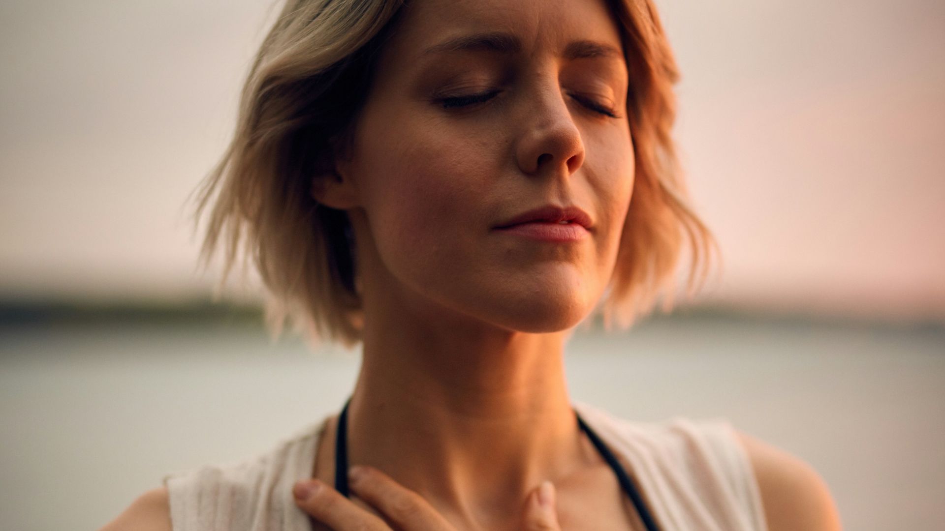 woman in white vest and black bikini with hand on chest