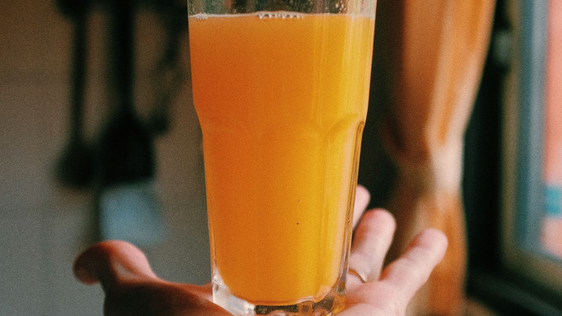 person holding clear drinking glass with yellow liquid