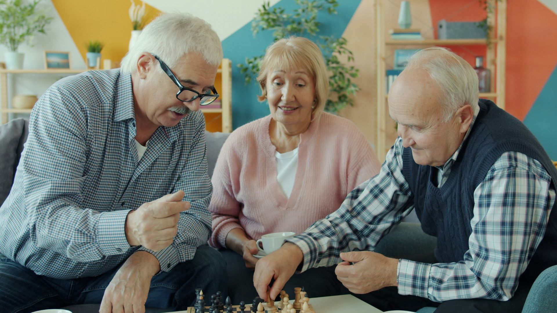 Three seniors playing chess together in a living room.