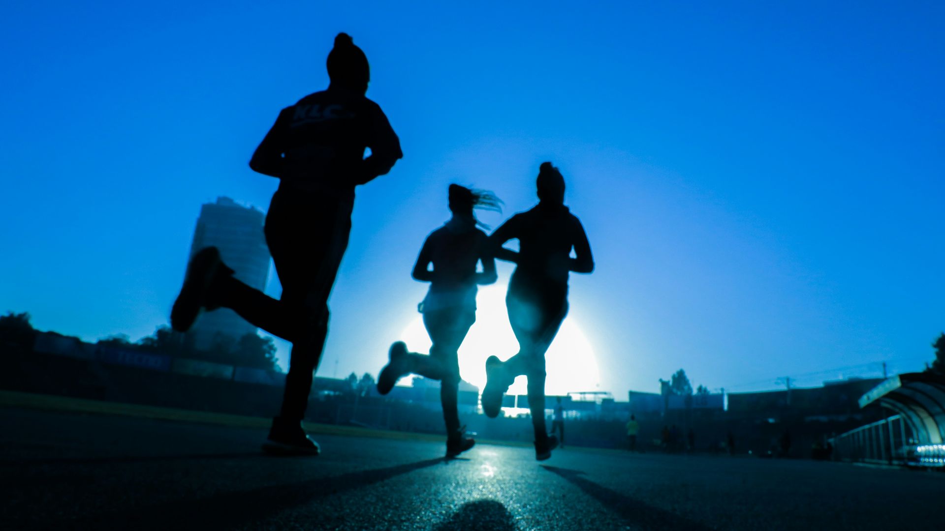 silhouette of three women running on grey concrete road