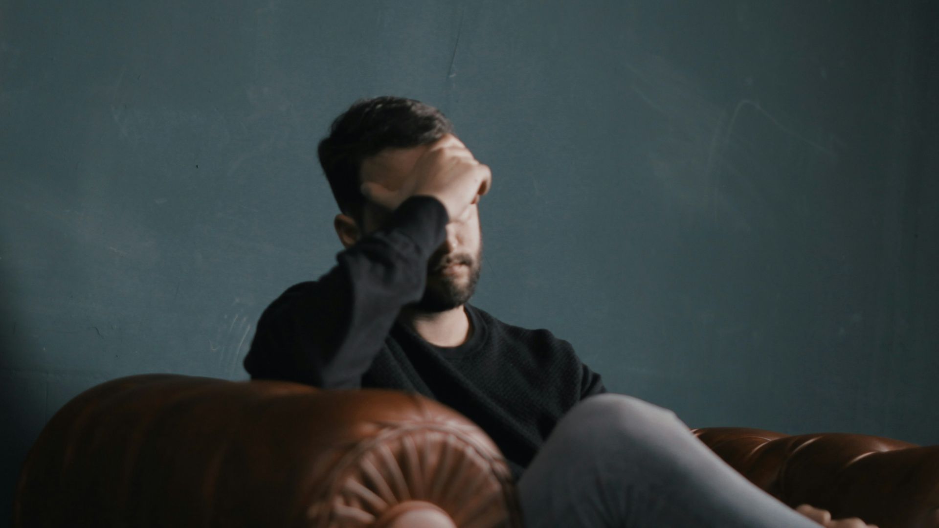 a man holds his head while sitting on a sofa