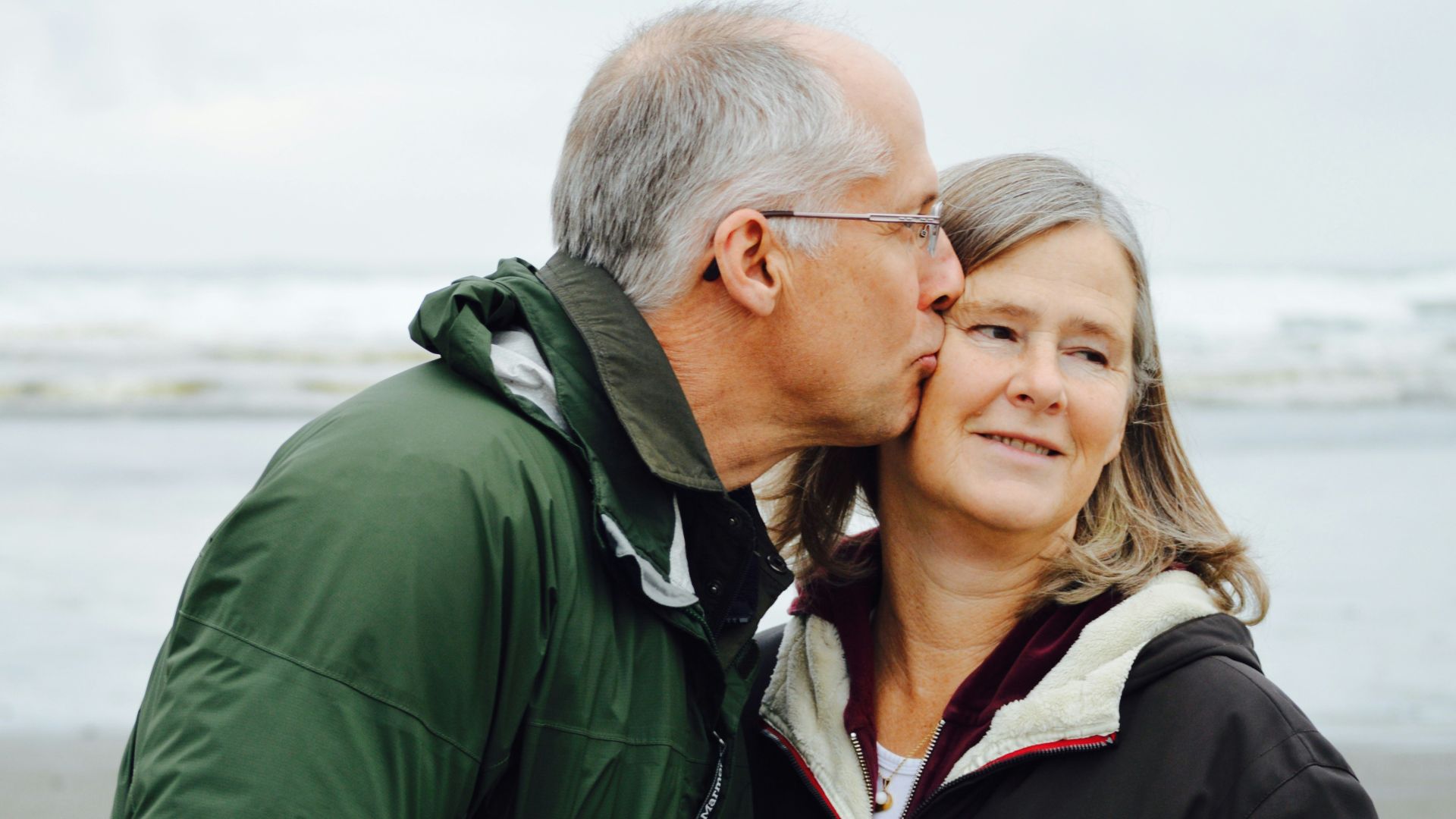 man kissing woman on check beside body of water