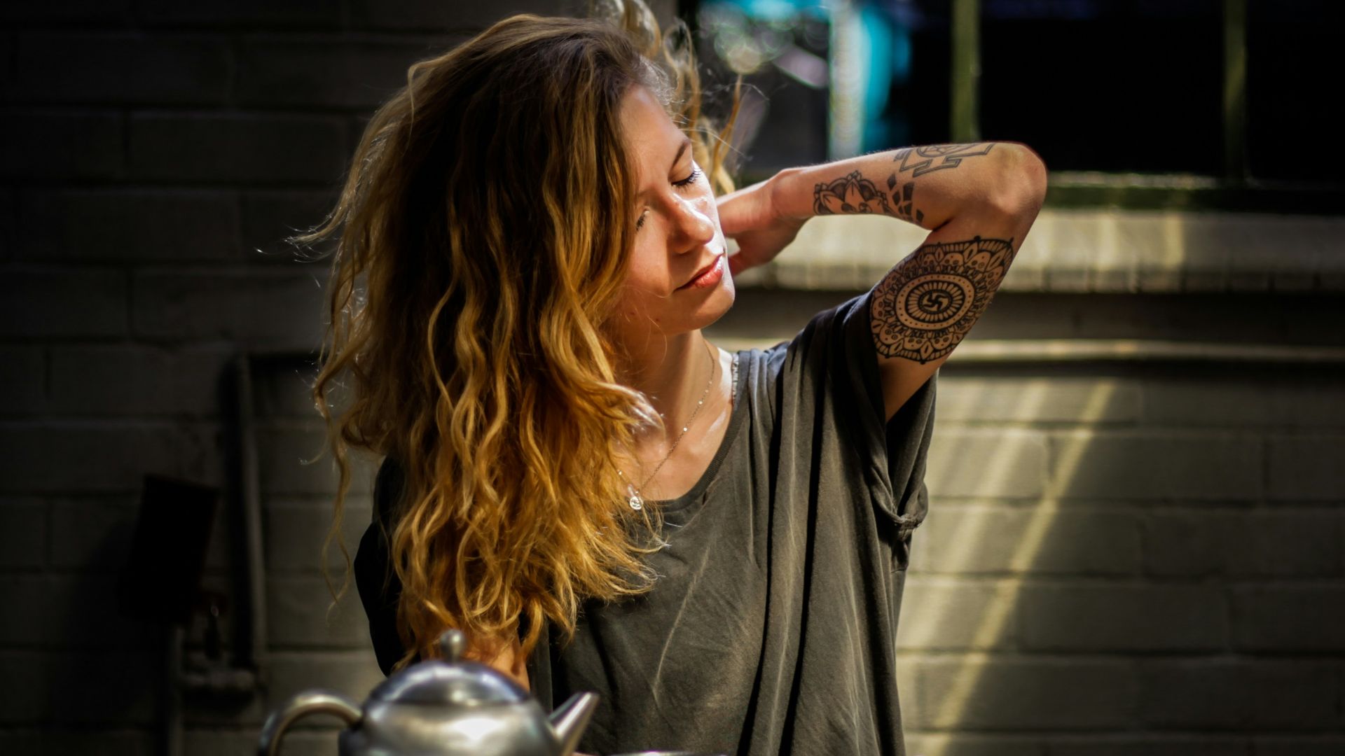 woman in gray top sitting beside gray tea pot and cup on brown wooden table