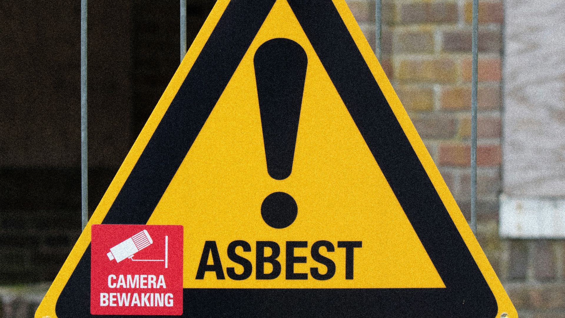 A yellow and black warning sign on a fence