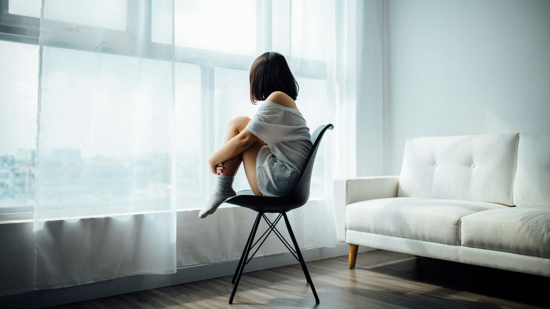woman sitting on black chair in front of glass-panel window with white curtains