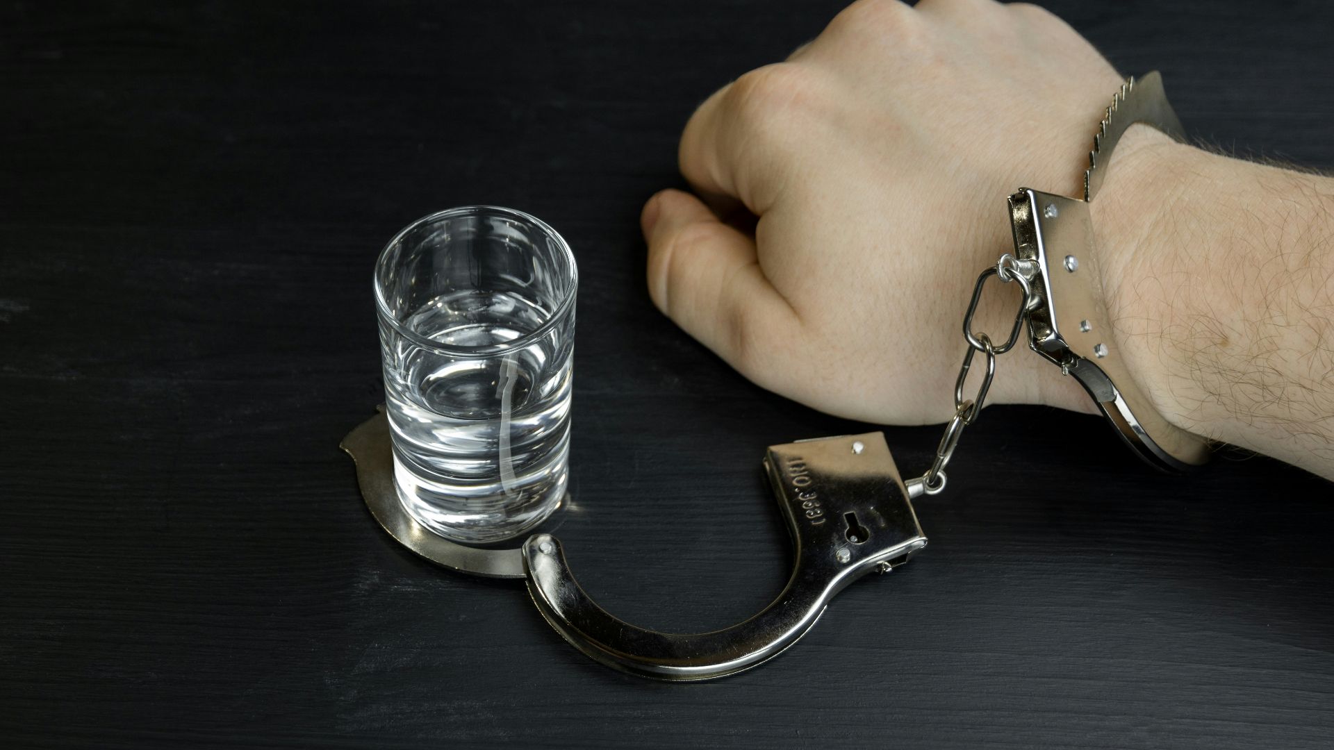 a man's hand with a handcuffs and a glass of water