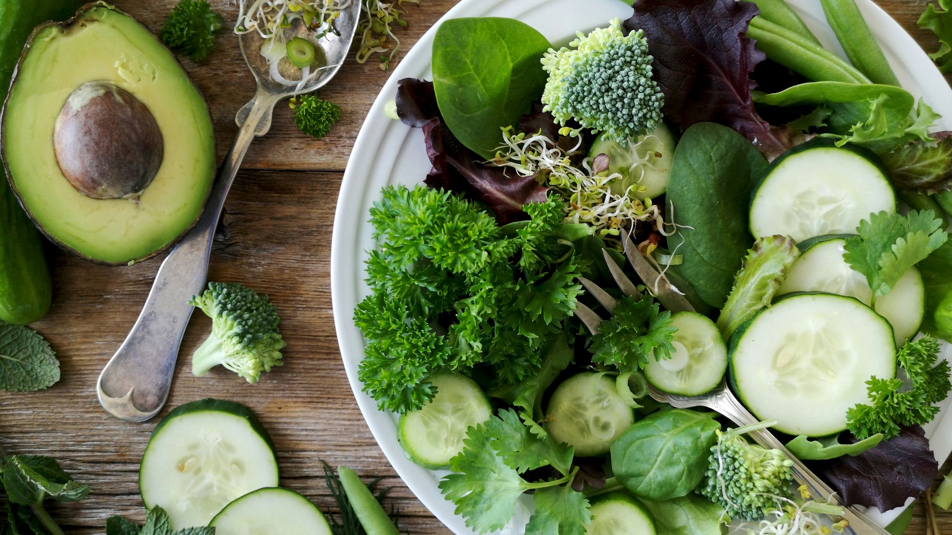 sliced broccoli and cucumber on plate with gray stainless steel fork near green bell pepper, snowpea, and avocado fruit
