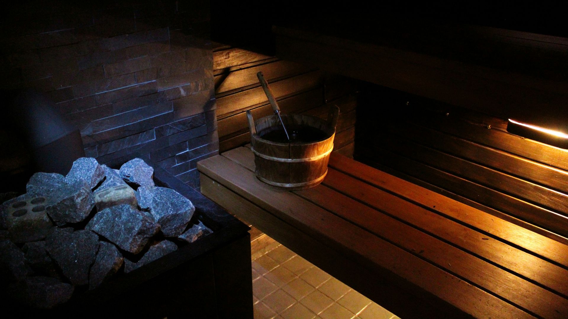 A sauna with rocks, a bucket, and wood.