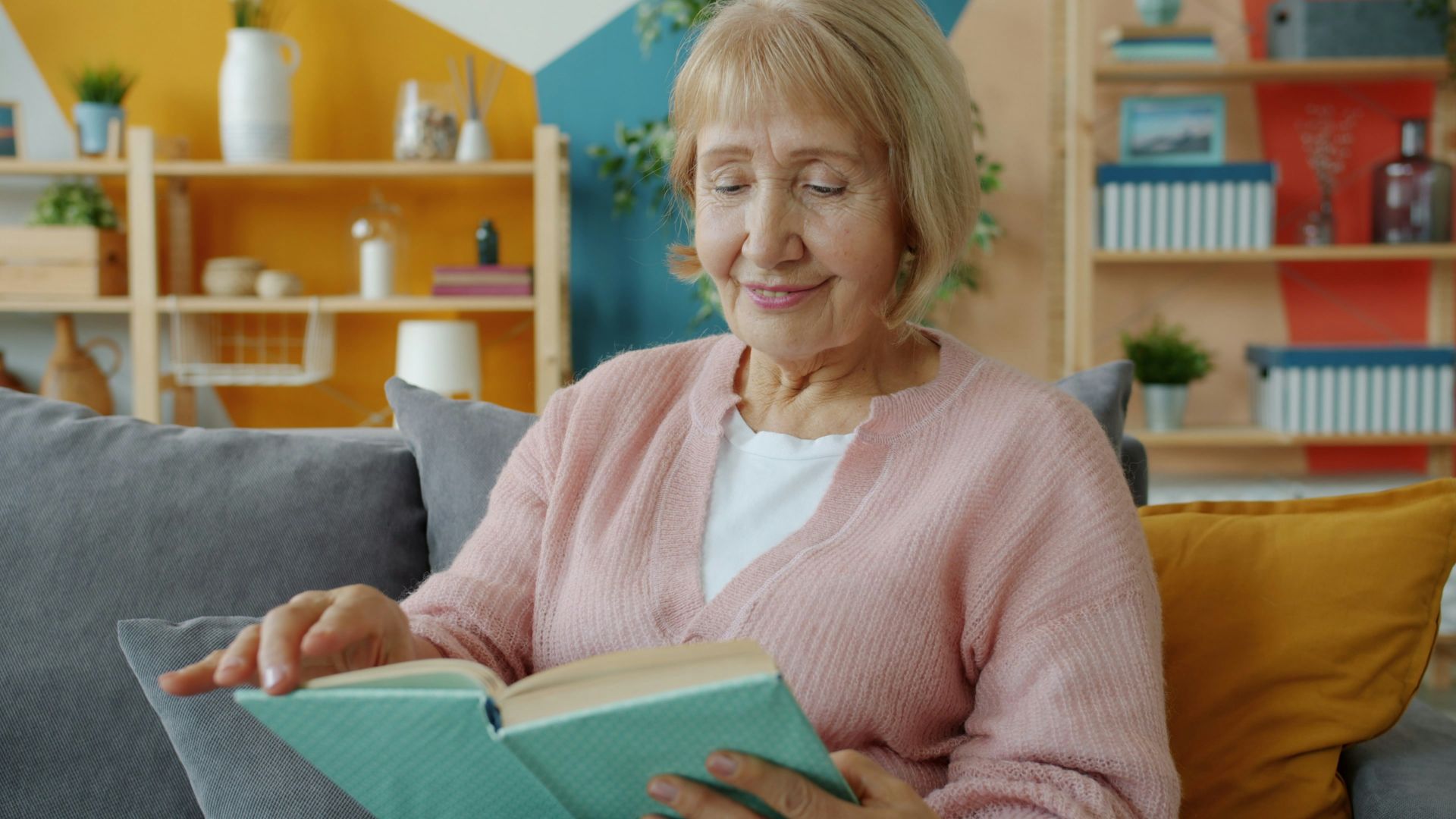 Elderly woman reading a book on a couch.