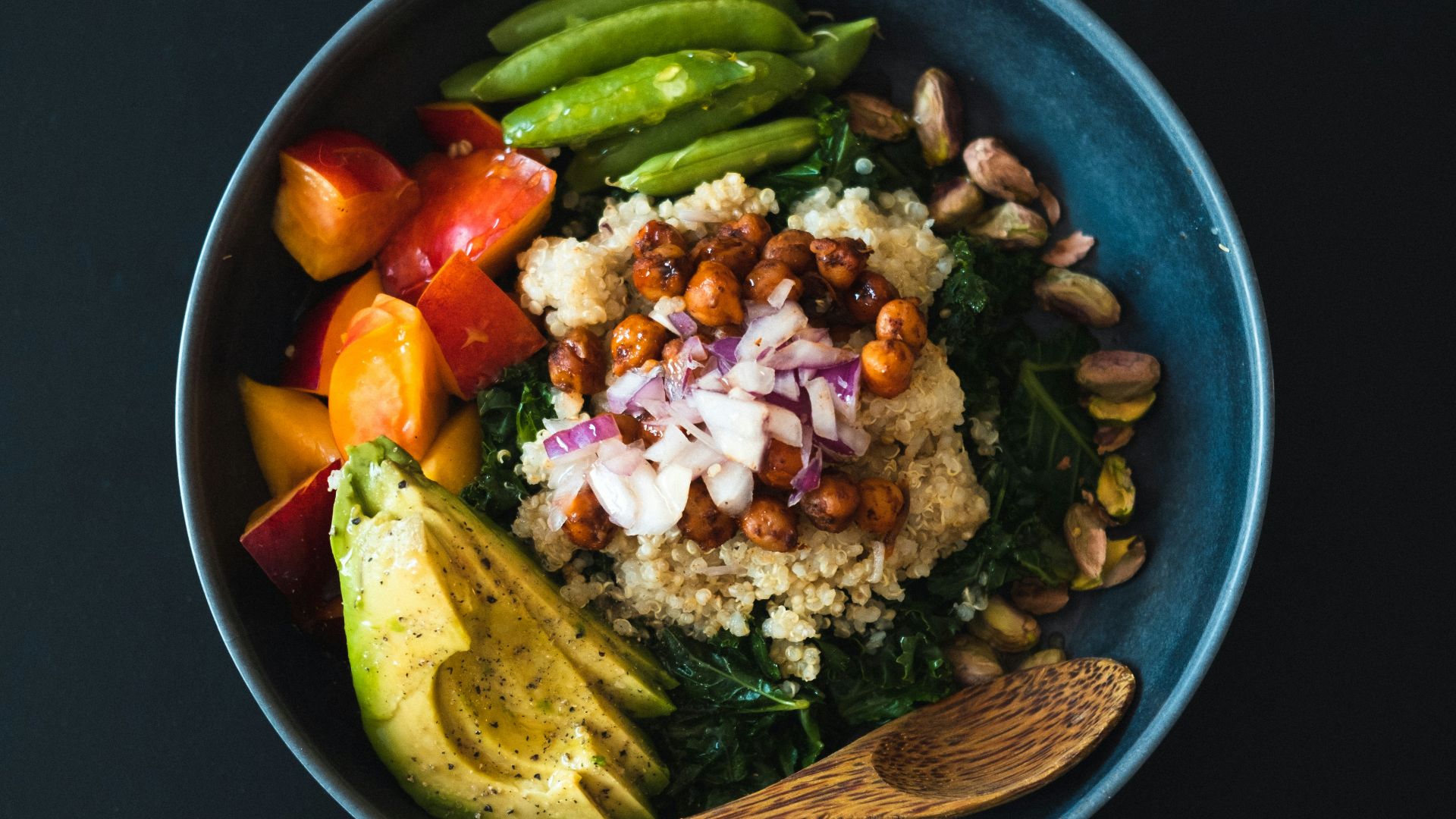 a blue bowl filled with vegetables and a wooden spoon