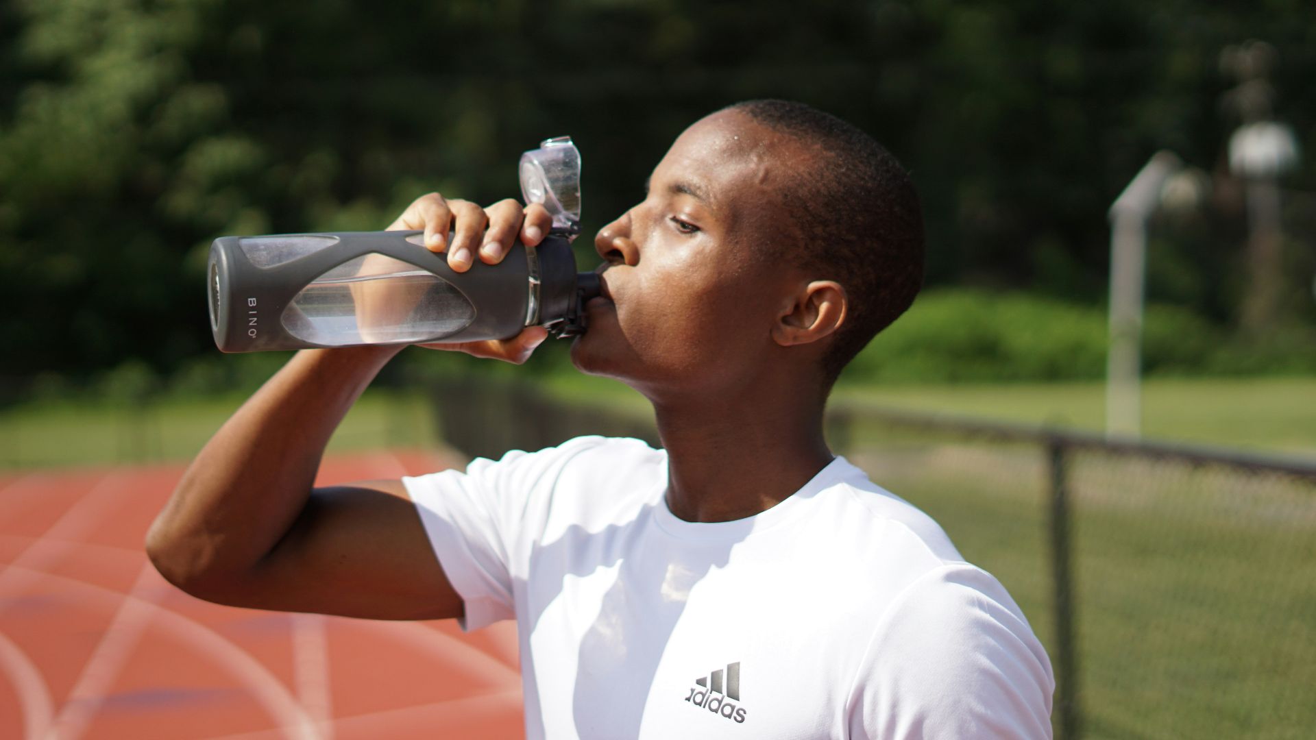 man in white crew neck t-shirt drinking from black sports bottle