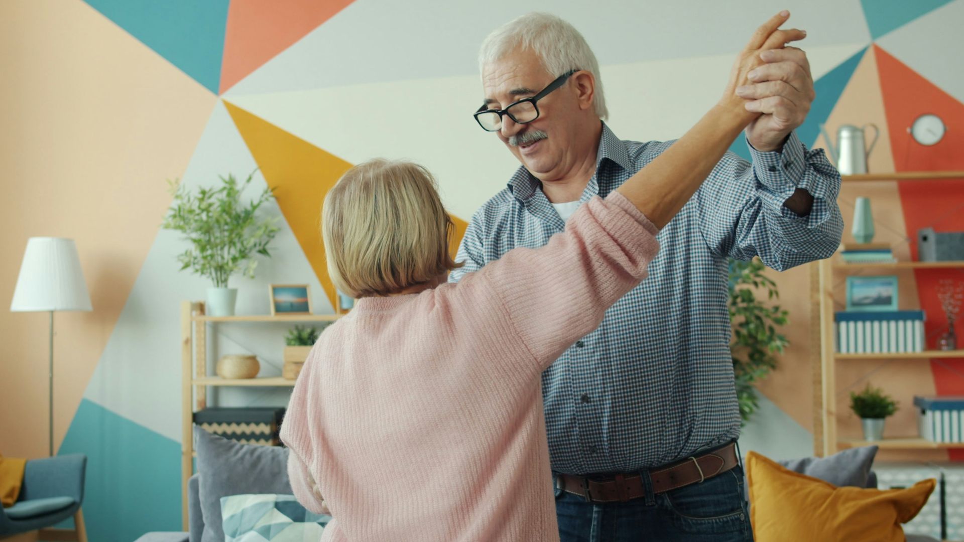 Elderly couple dancing happily in a colorful living room.